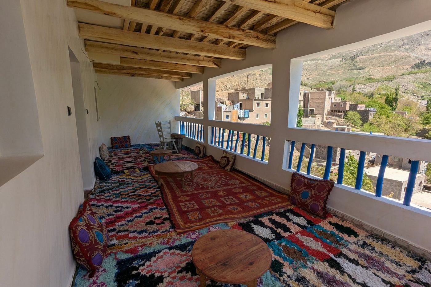 A terrace of an independent Moroccan guesthouse, laid with Berber rugs and low tables, looking out over a mountain village
