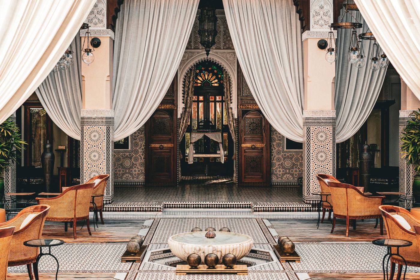 The tiled courtyard of a Moroccan riad, with carved plasterwork, drapes and a marble fountain